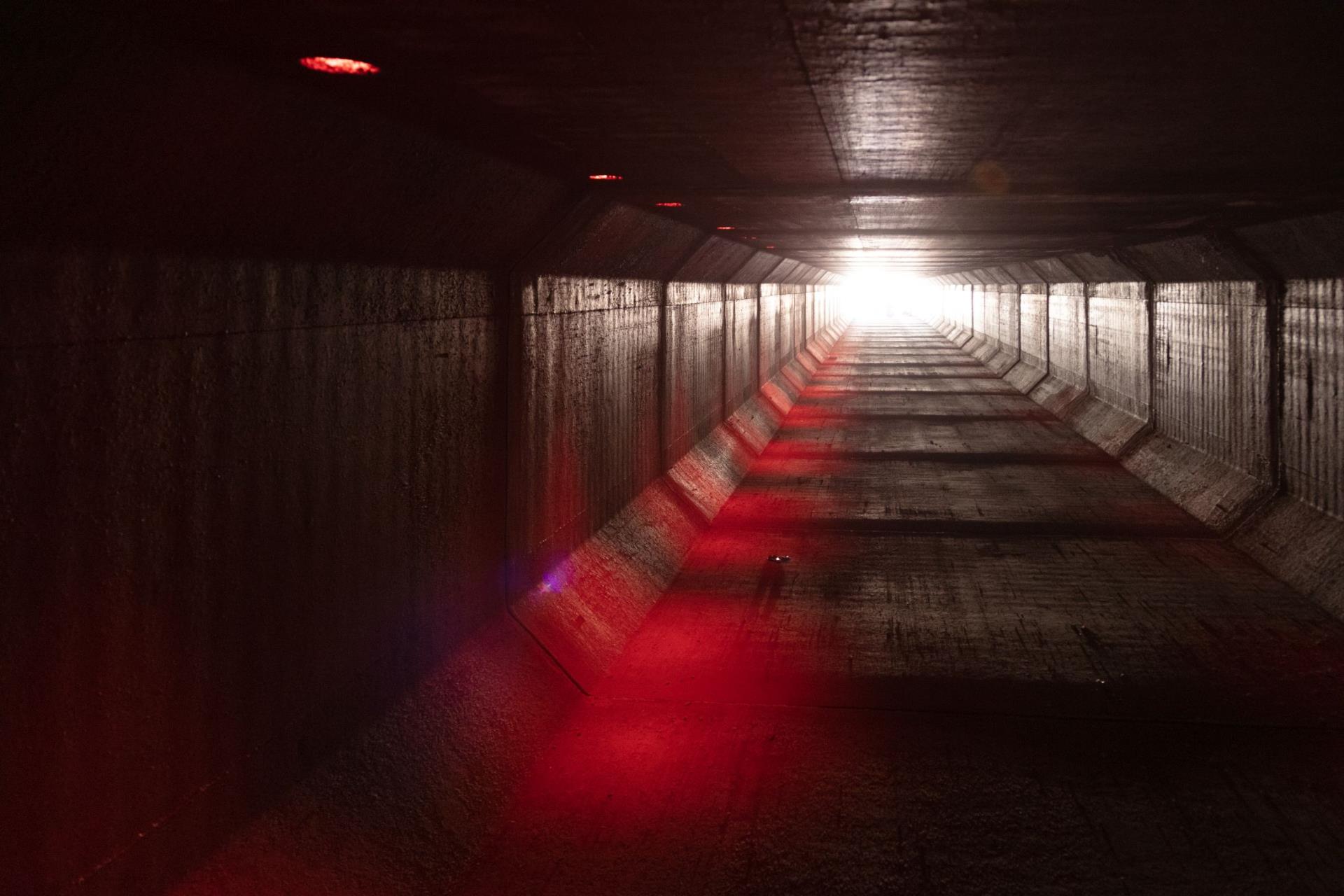 Red lights shine inside of a storm drain underground.